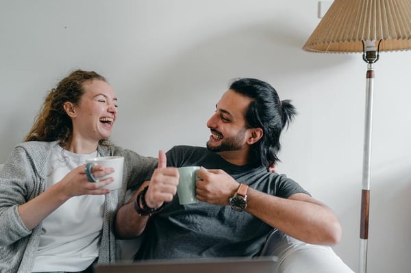 A couple sitting on the couch talking about the signs of ADHD together. They are laughing and drinking coffee.