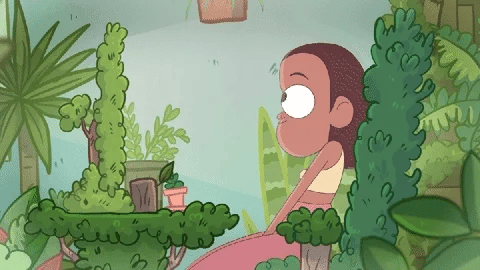A gif showing an animation of a BIPOC person sitting at a desk in front of a glowing screen. The desk is surrounded by different green plants, including plants that have overgrown the actual desk and the stand and casing of the screen. The person is looking around, then smiles and squeezes their eyes shut, tilting their head, while pulling up their shoulders in a gesture of happy excitement.