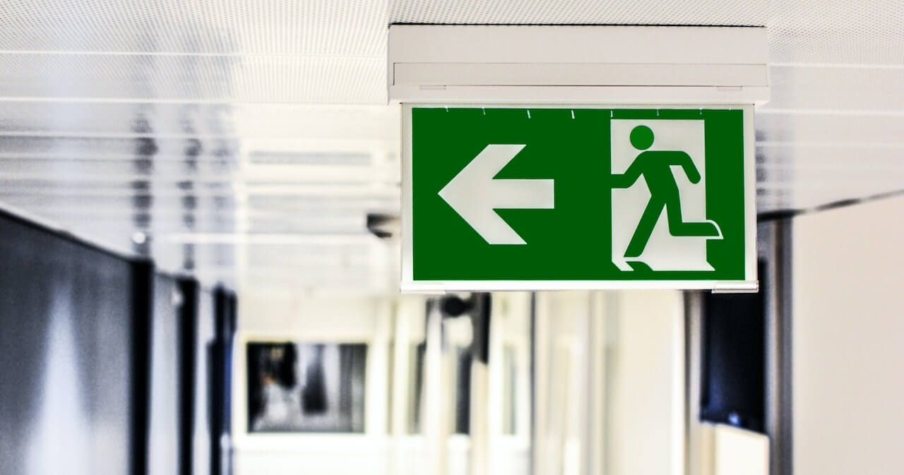 A sign showing a person running out of a door. The sign is green and has an arrow pointing in the direction the person is running.